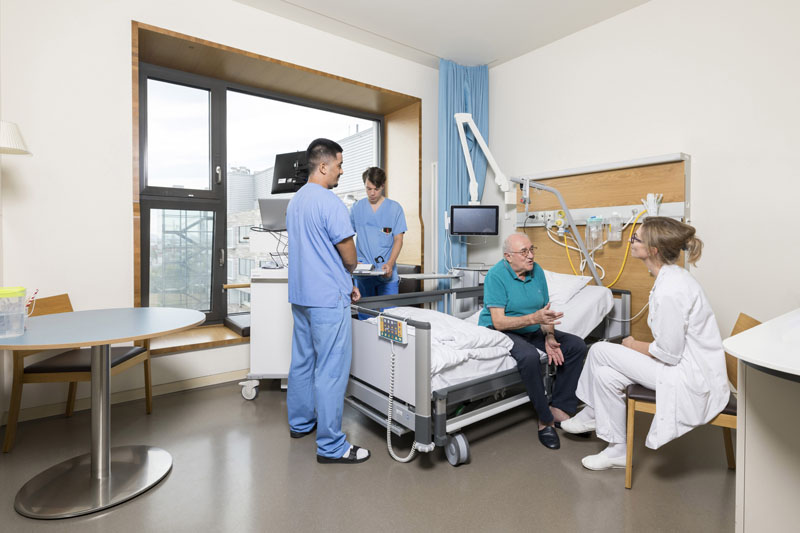 Klinik Floridsdorf interdisziplinäres Team bei Visite im Gespräch mit einem neurologischen Patienten auf der Station